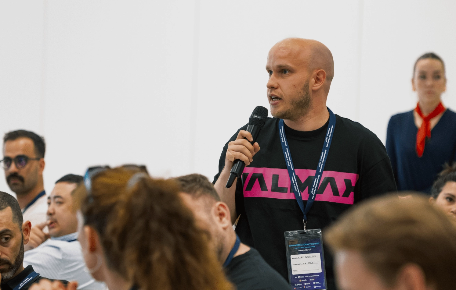 Man speaking at event in Valmax t-shirt Man with mic in Valmax t-shirt at conference